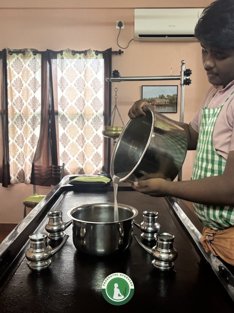 A therapist at Prakruthi Ayurveda fills a fermented liquid called Dhanyamla Dhara from a bigger metal vessel into a smaller one. It is placed on a massage table together with four small vessels that will be used to pour the liquid finally onto a person
